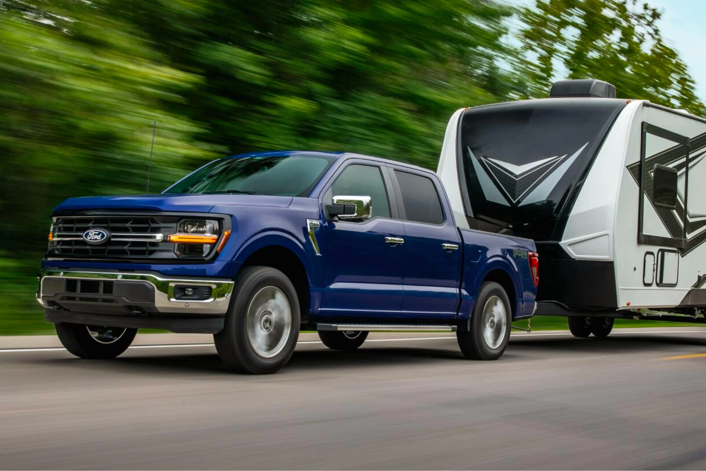 A blue 2026 Ford F-150 XLT towing a travel trailer along a highway