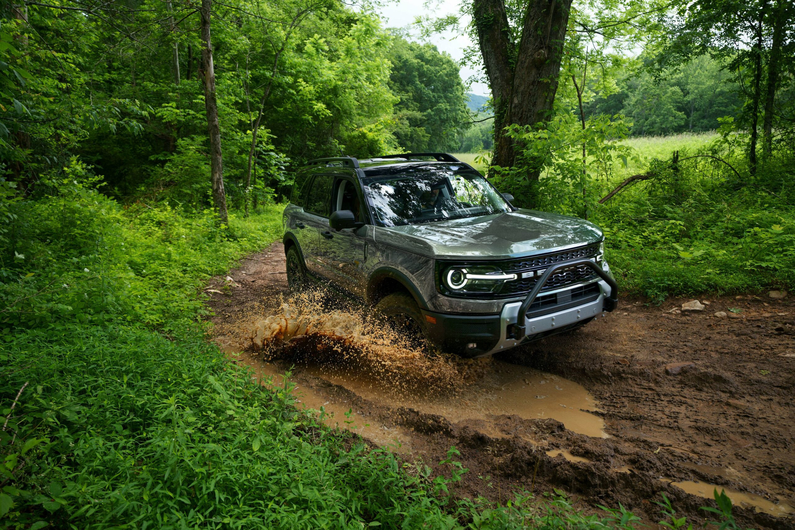 A 2026 Ford Bronco Sport driving through mud on a wooded trail