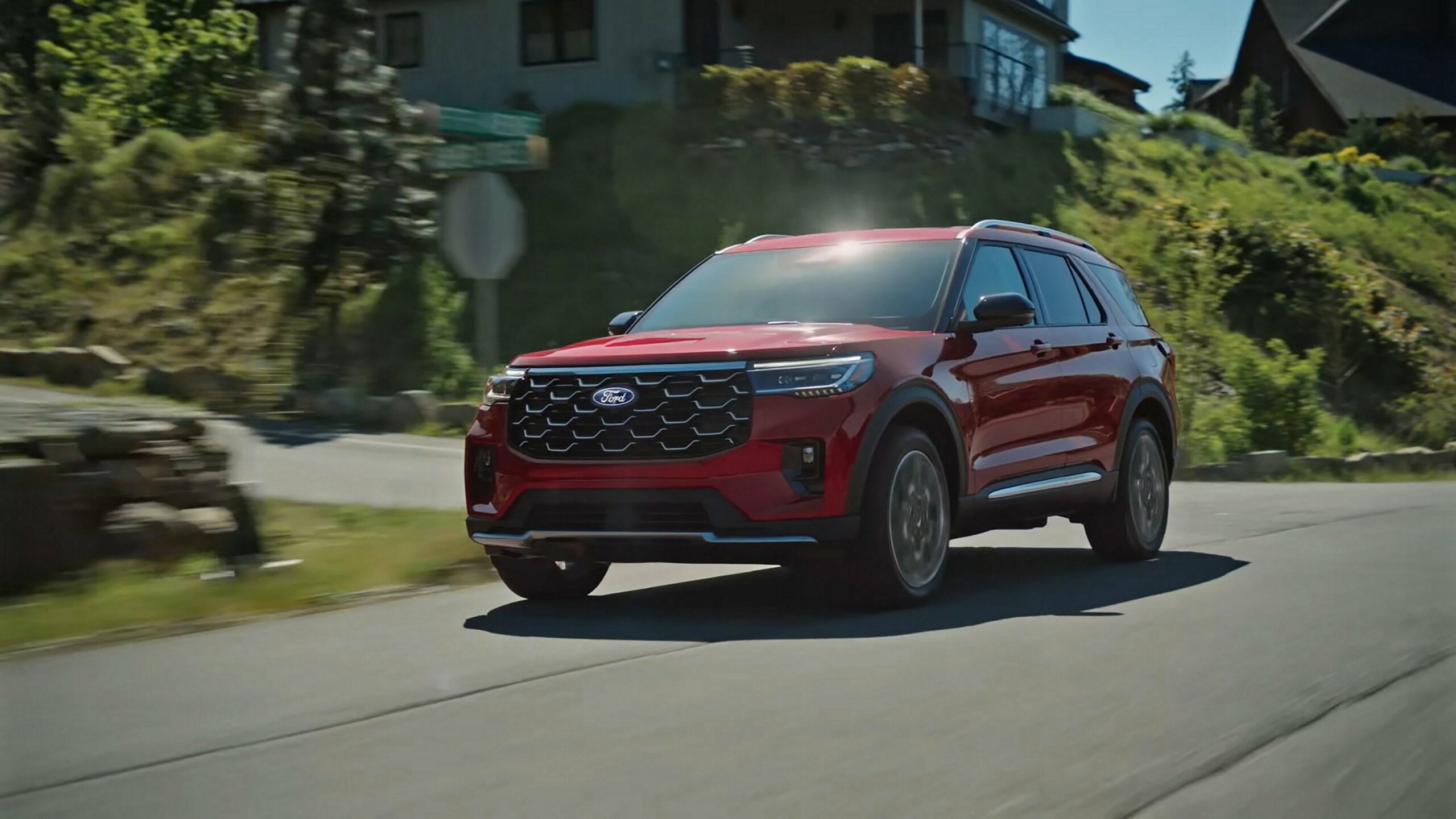 A red 2027 Ford Explorer on a two-lane road through forested hills