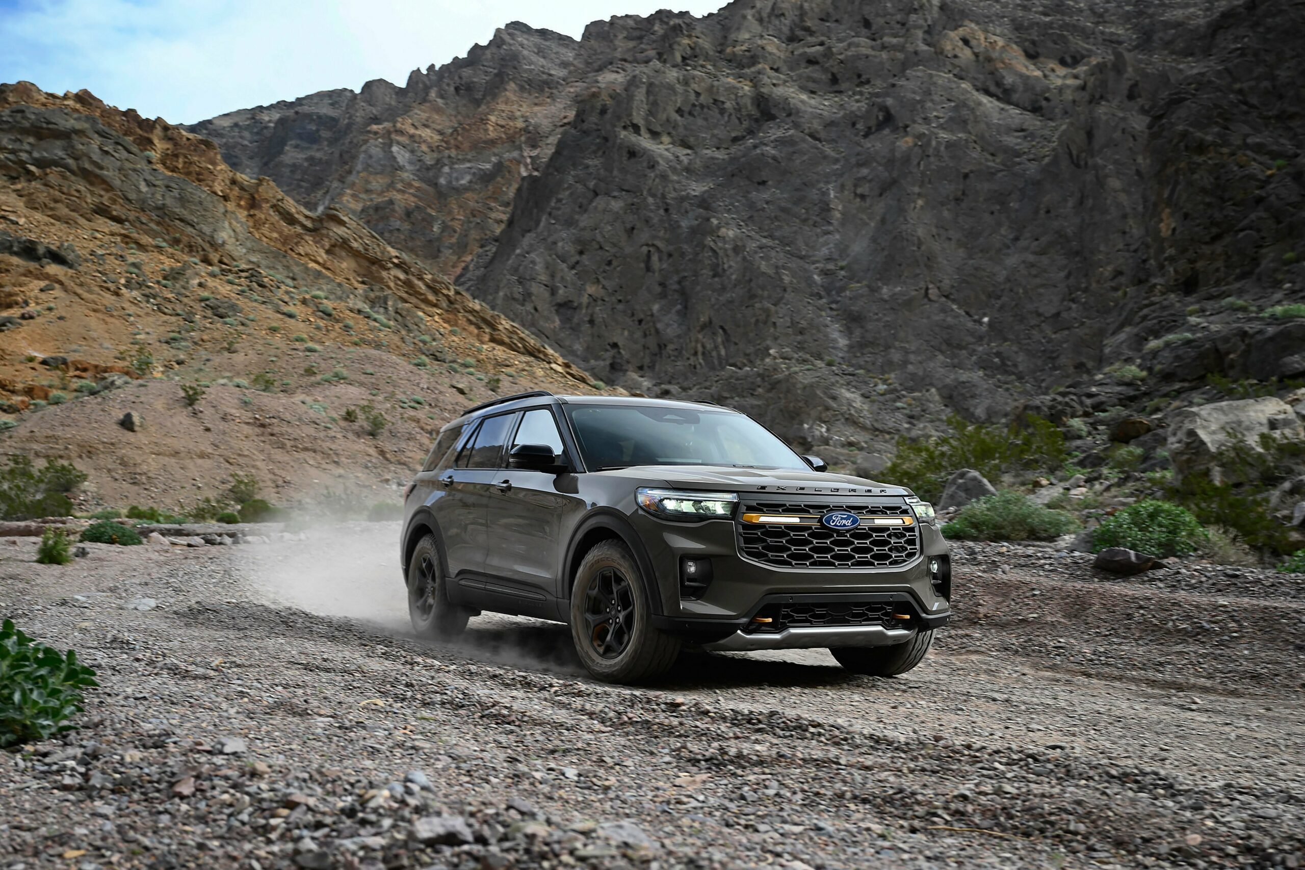 A gray 2027 Ford Explorer Tremor raising dust on a gravel track below a rock face