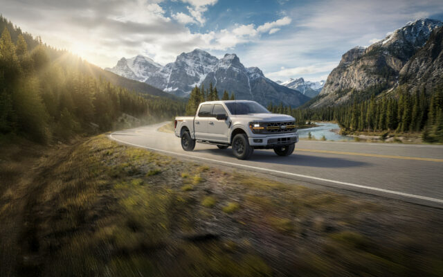 A white 2026 Ford F-150 Tremor on a curving mountain road beside a river, snow-capped peaks behind