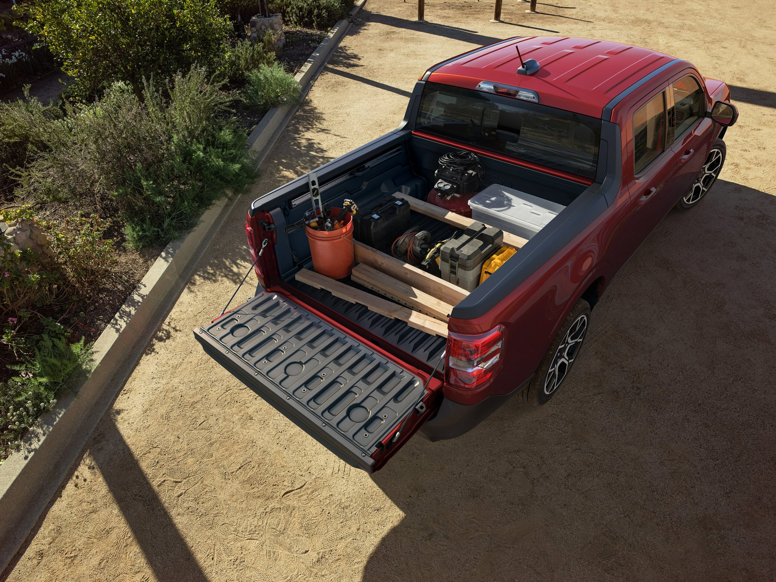 The open bed of a red 2026 Ford Maverick loaded with lumber, a bucket, a cooler and a generator, tailgate down