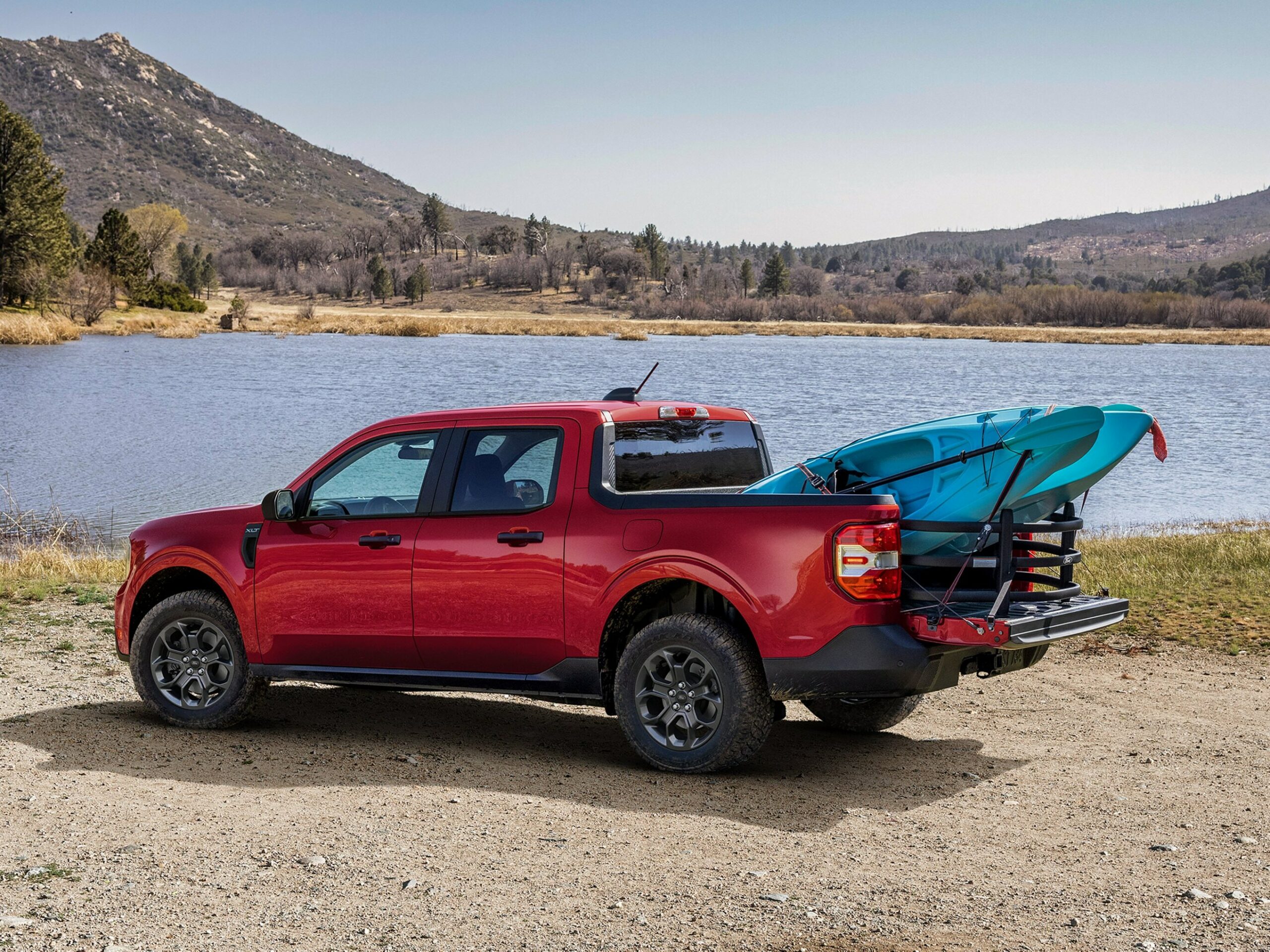 A red 2026 Ford Maverick beside a lake with a blue kayak resting on the lowered tailgate