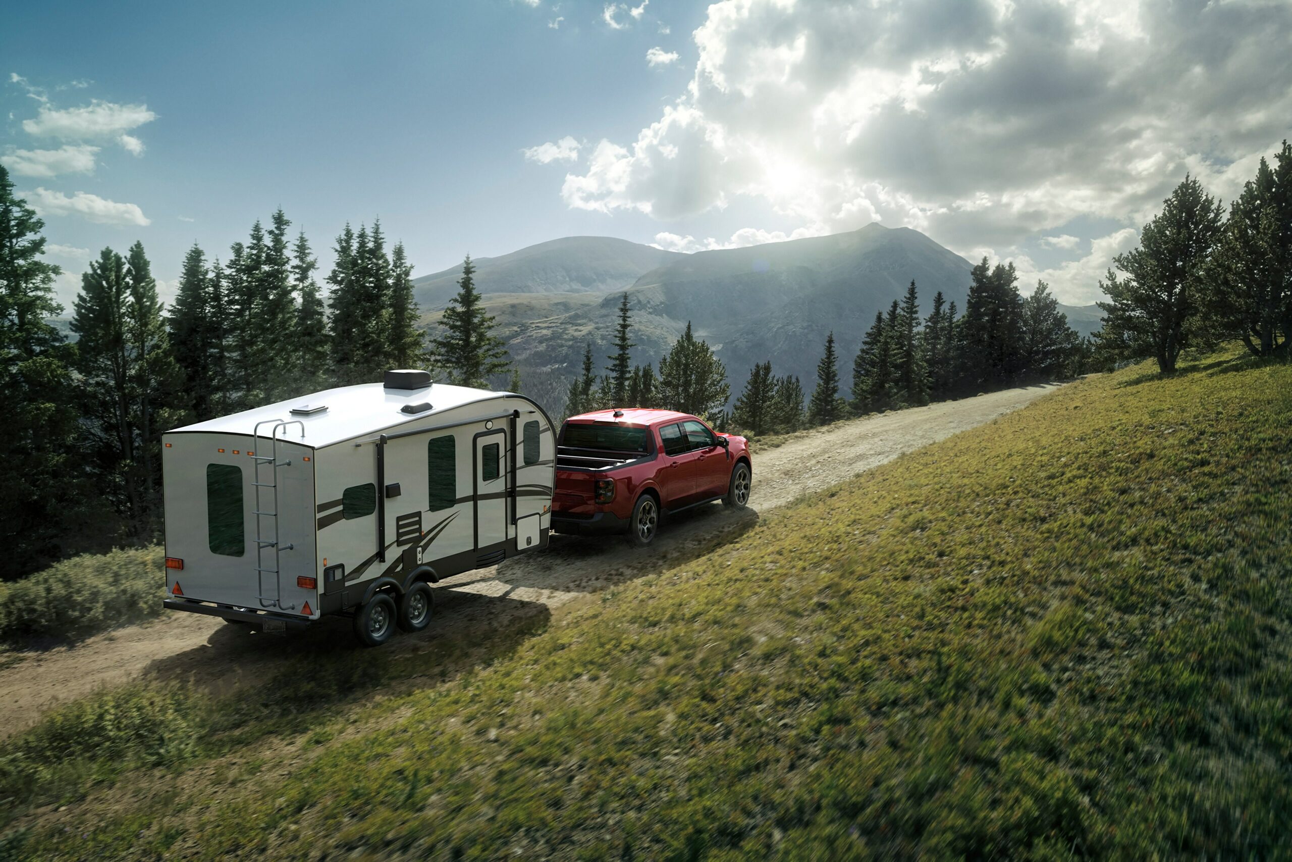 A red 2026 Ford Maverick towing a white travel trailer up a grassy hill below pine trees and mountains