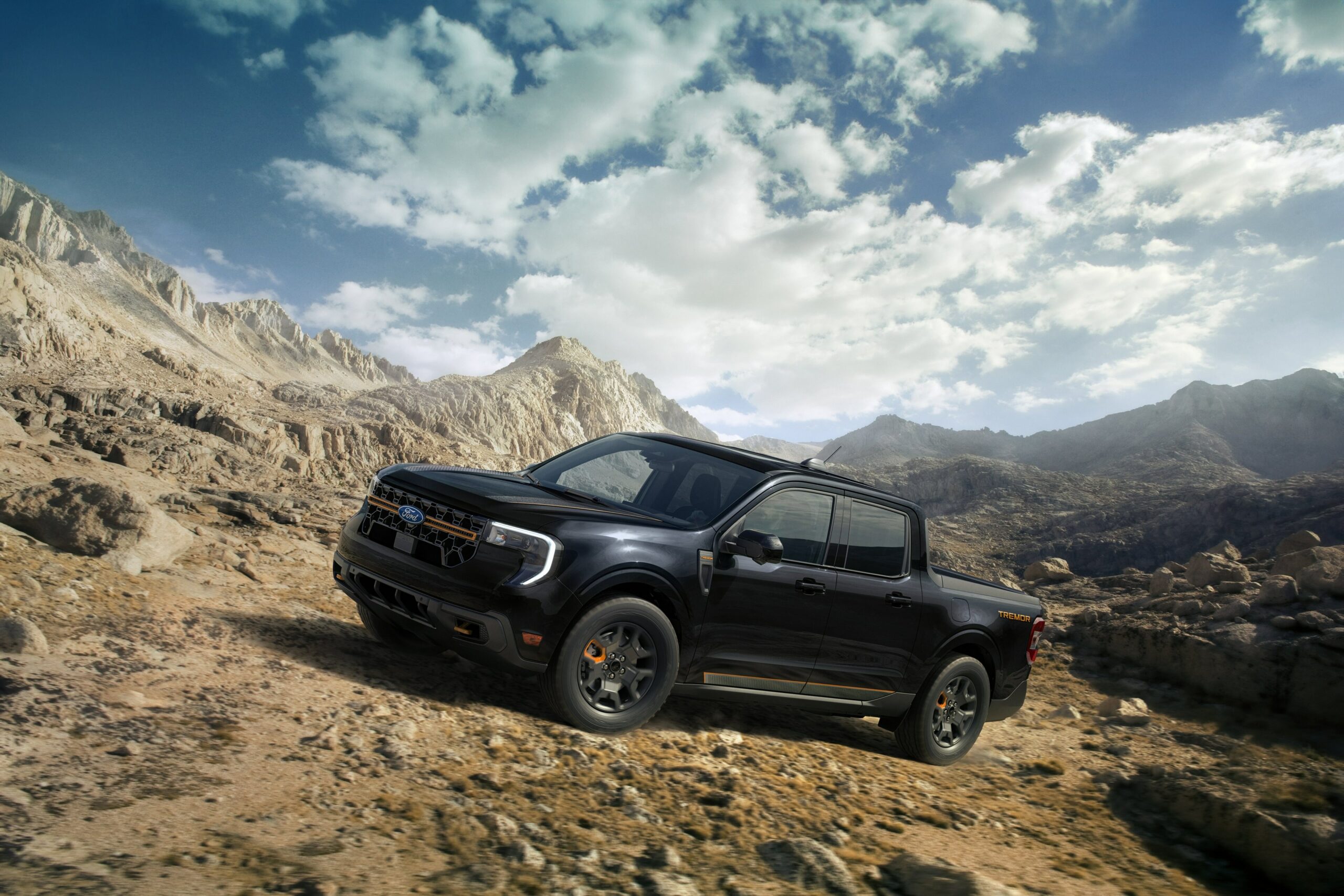 A black 2026 Ford Maverick Tremor with orange tow hooks on a rocky desert trail below jagged peaks