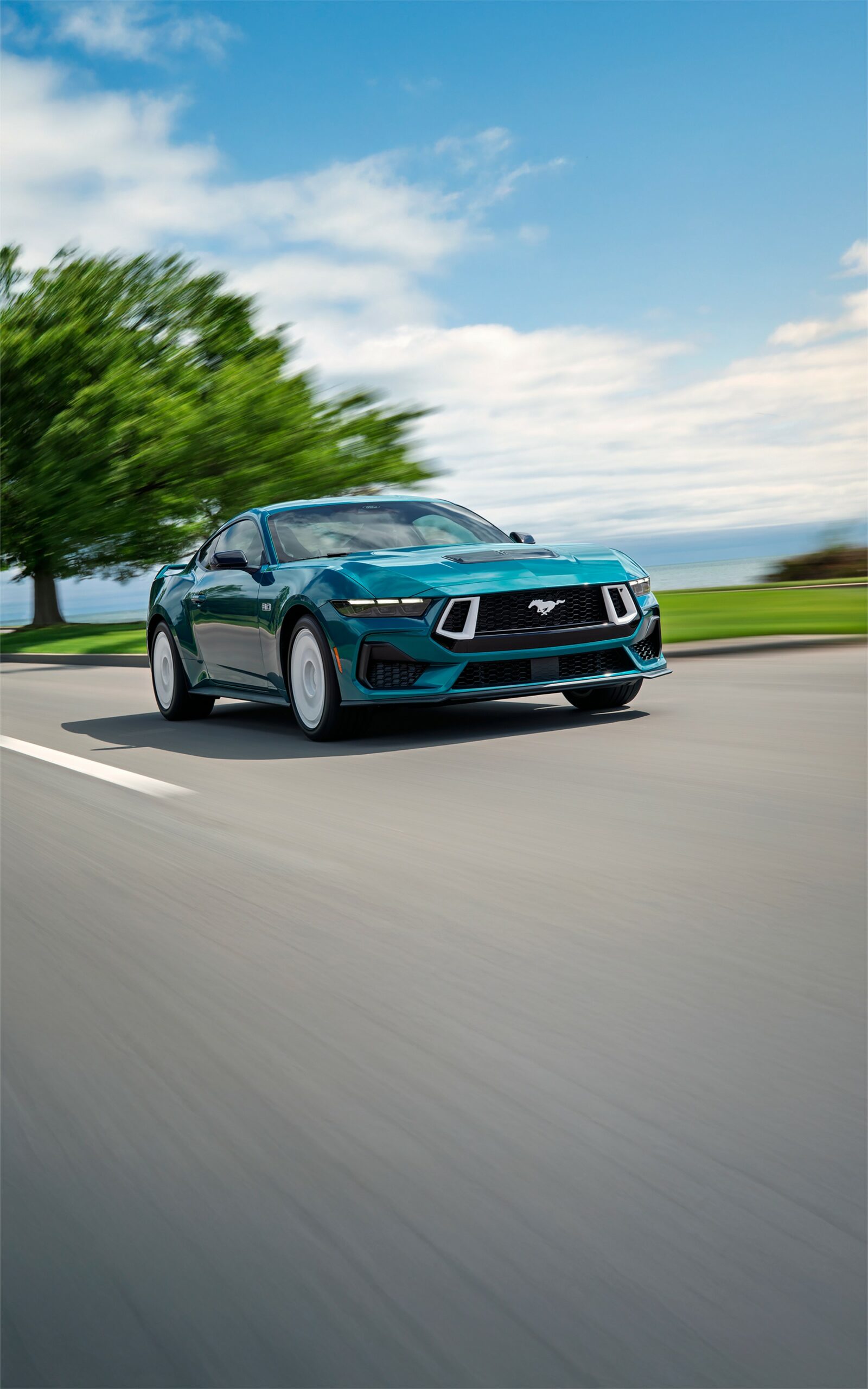 A teal 2026 Ford Mustang GT Premium driving on a tree-lined road