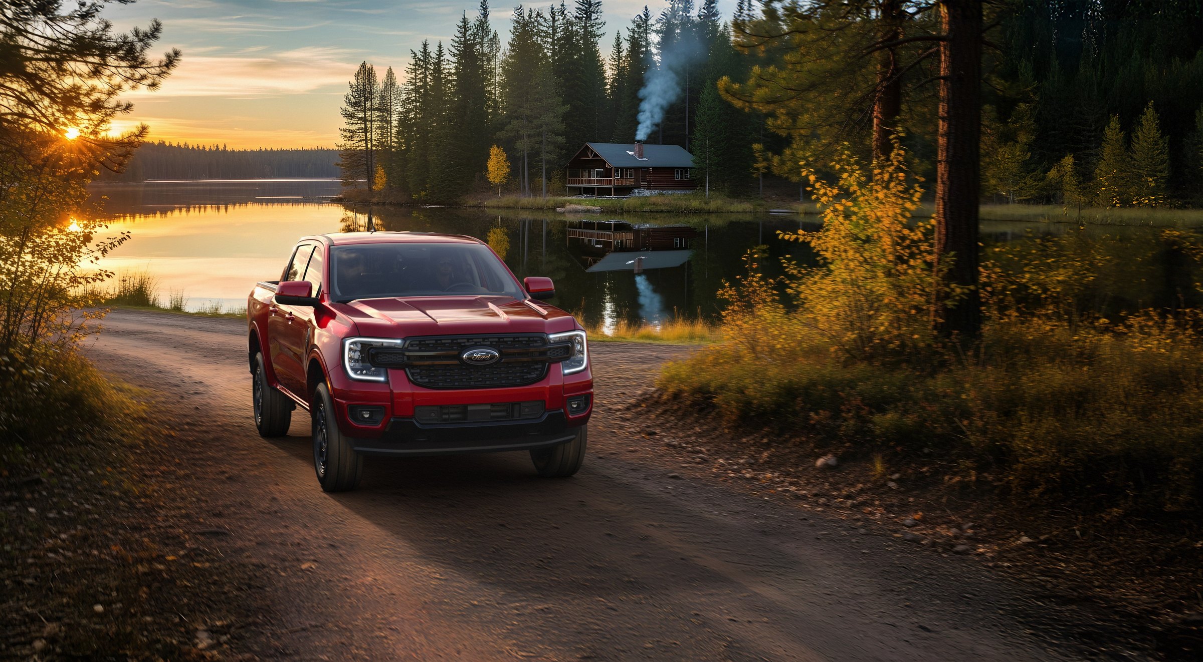 A Ruby Red 2026 Ford Ranger with a blacked-out grille parked on a dirt track beside a still lake at sunset, a cabin and pine forest on the far shore