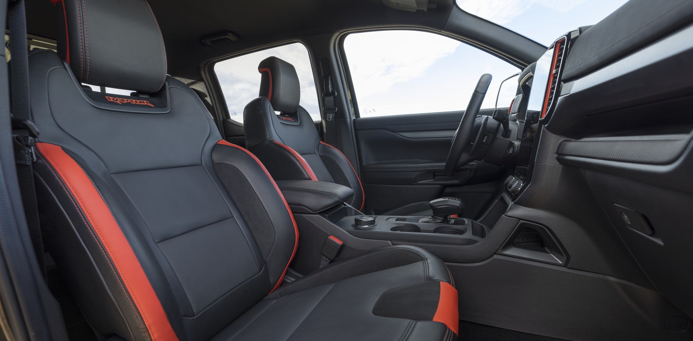 The front seats of a 2026 Ford Ranger Raptor in ebony with orange bolster accents and Raptor embroidered into the headrests