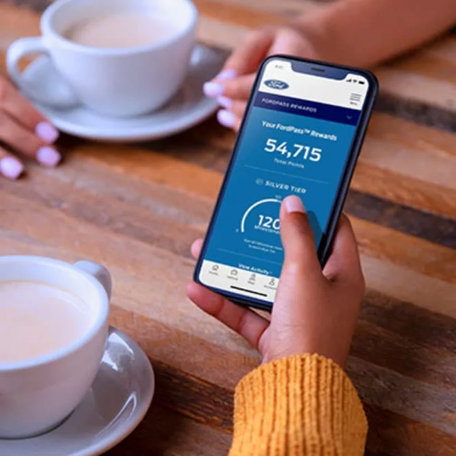 A phone showing a Ford Rewards Points balance and Silver Tier status, on a café table beside coffee cups