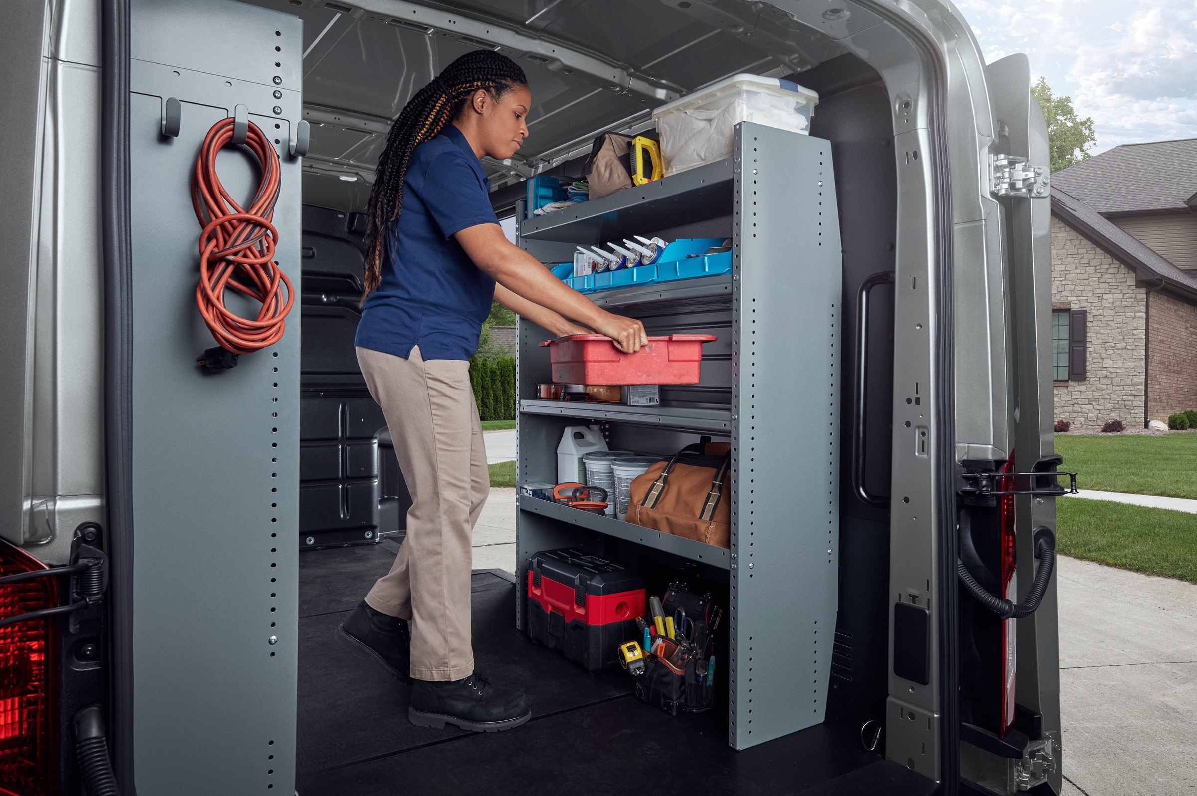 A worker placing a red toolbox onto metal shelving racks inside a Ford Transit