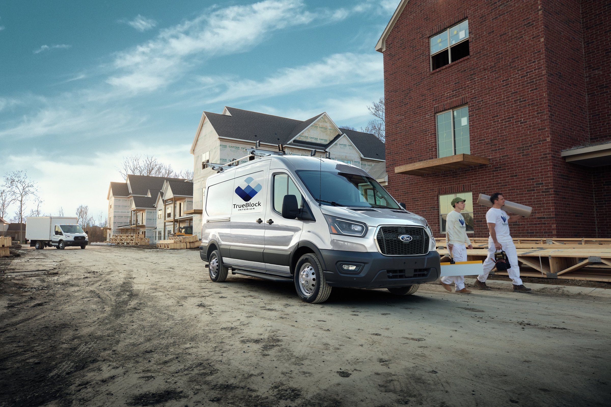 A white high-roof Ford Transit cargo van with a company logo parked at a construction site