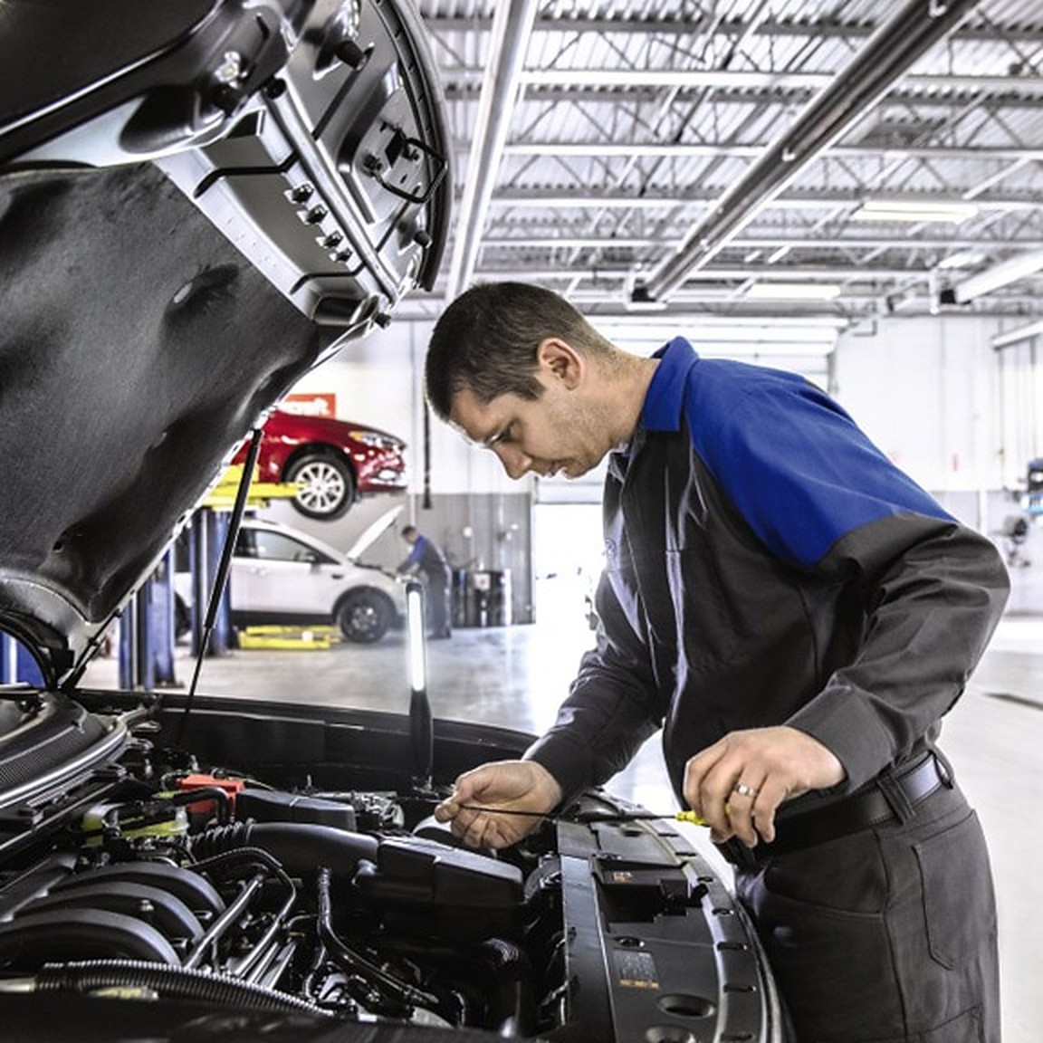 A Ford technician working at an open engine bay in a service bay